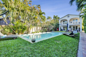 Resort-style heated pool courtyard at 1050 NE 33rd Street in Oakland Park featuring tropical landscaping, private fenced yard, and two-story home with balcony overlooking the pool.