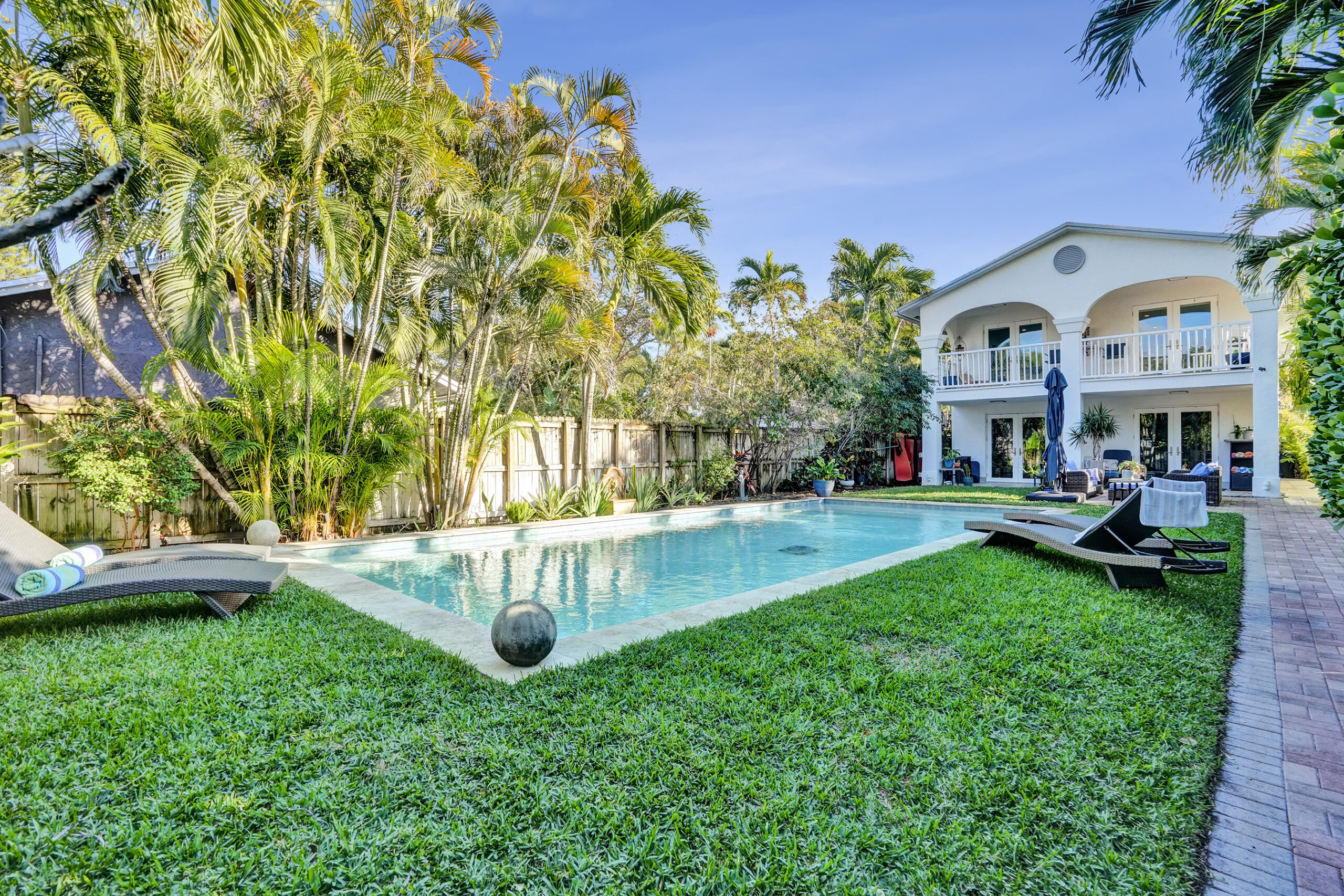 Oakland Park Pool Home – 1050 NE 33rd Street Resort-style heated pool courtyard at 1050 NE 33rd Street in Oakland Park featuring tropical landscaping, private fenced yard, and two-story home with balcony overlooking the pool.